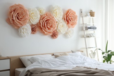 Photo of Beautiful decorative paper flowers on wall in bedroom