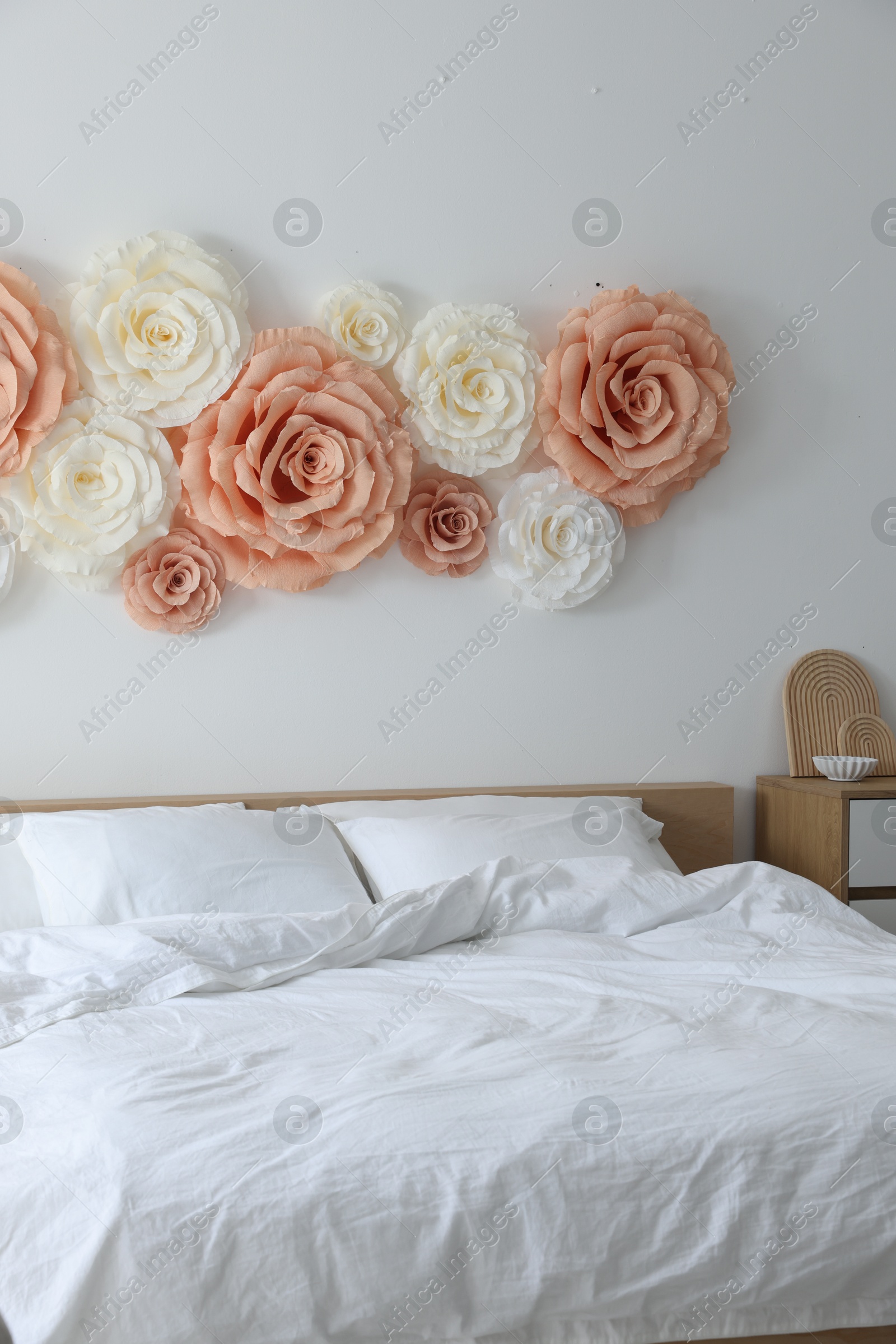 Photo of Beautiful decorative paper flowers on wall in bedroom