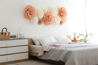 Photo of Beautiful decorative paper flowers on wall in bedroom