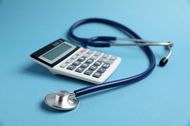 Photo of Stethoscope and calculator on light blue background, closeup