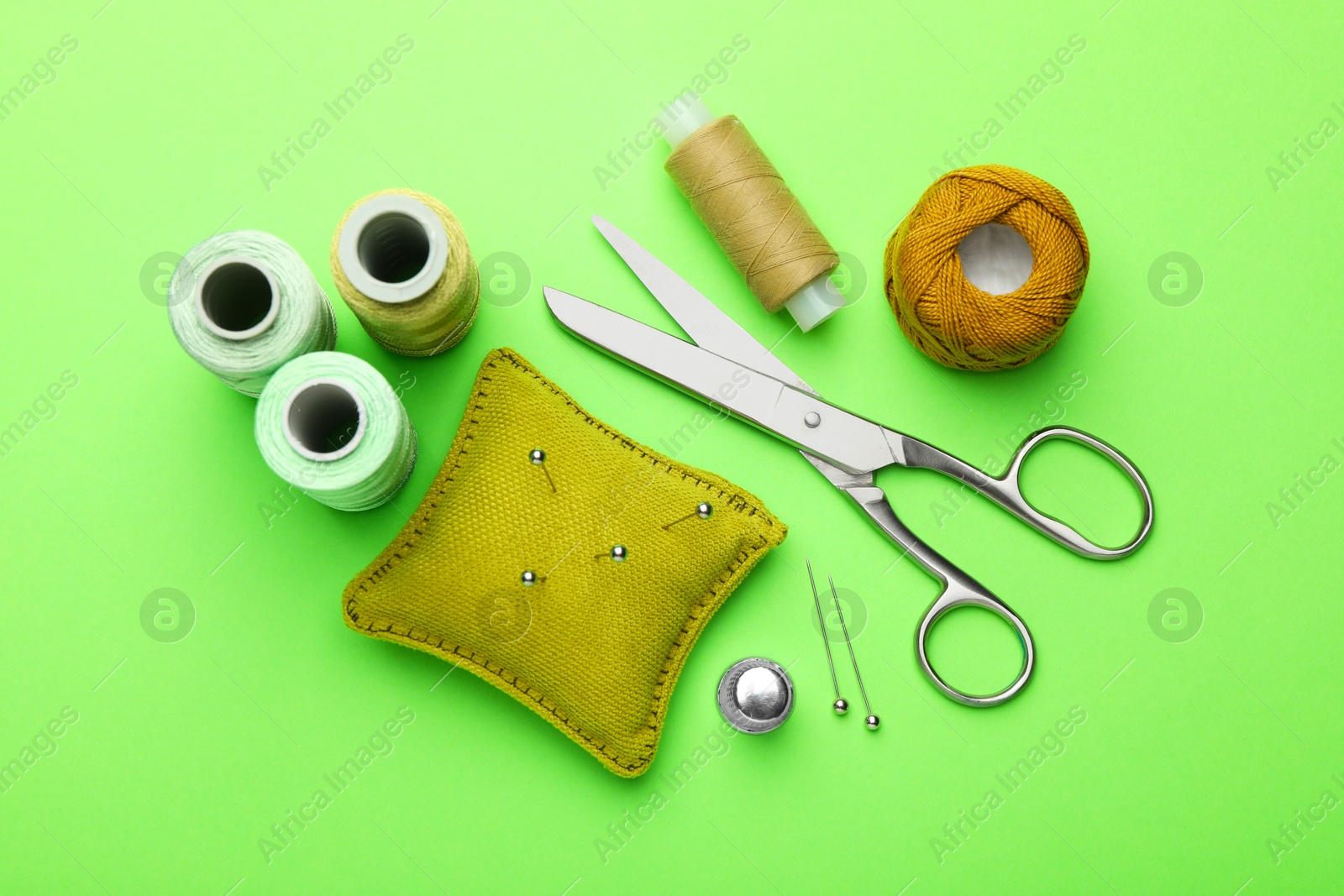 Photo of Different sewing supplies on green background, flat lay