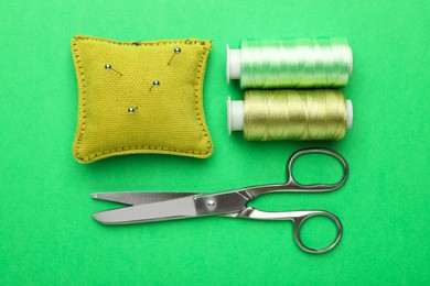 Different sewing supplies on green background, flat lay