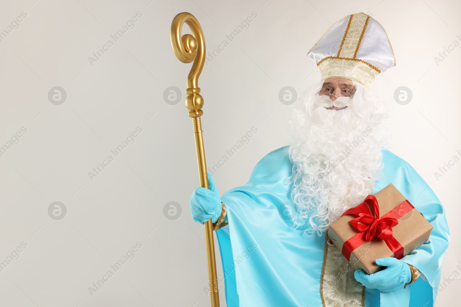 Photo of Saint Nicholas with Christmas gift and crozier on gray background, space for text