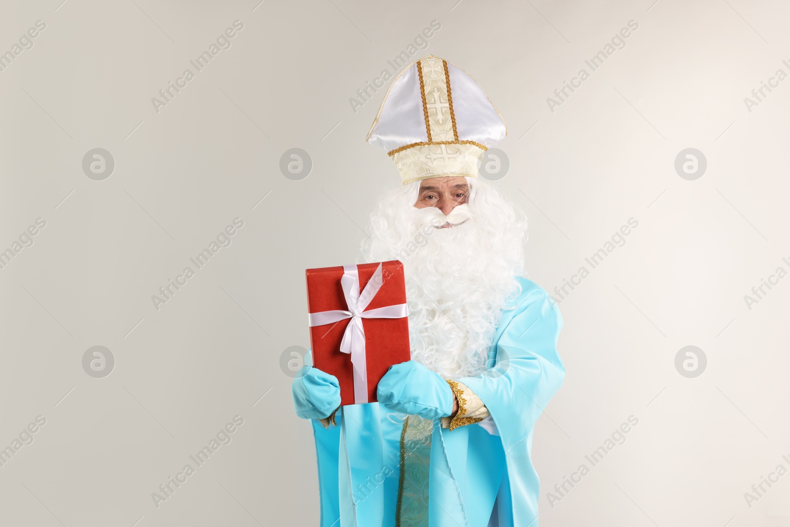 Photo of Saint Nicholas with Christmas gift on gray background