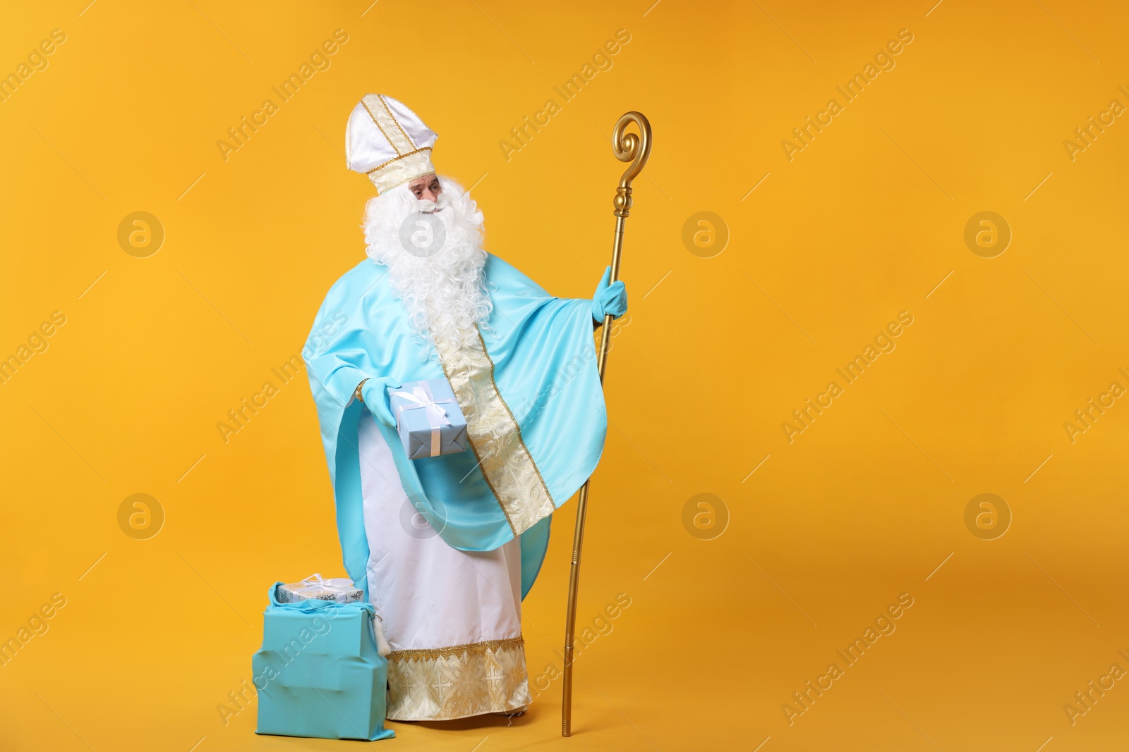 Photo of Saint Nicholas with Christmas gift and crozier on orange background, space for text