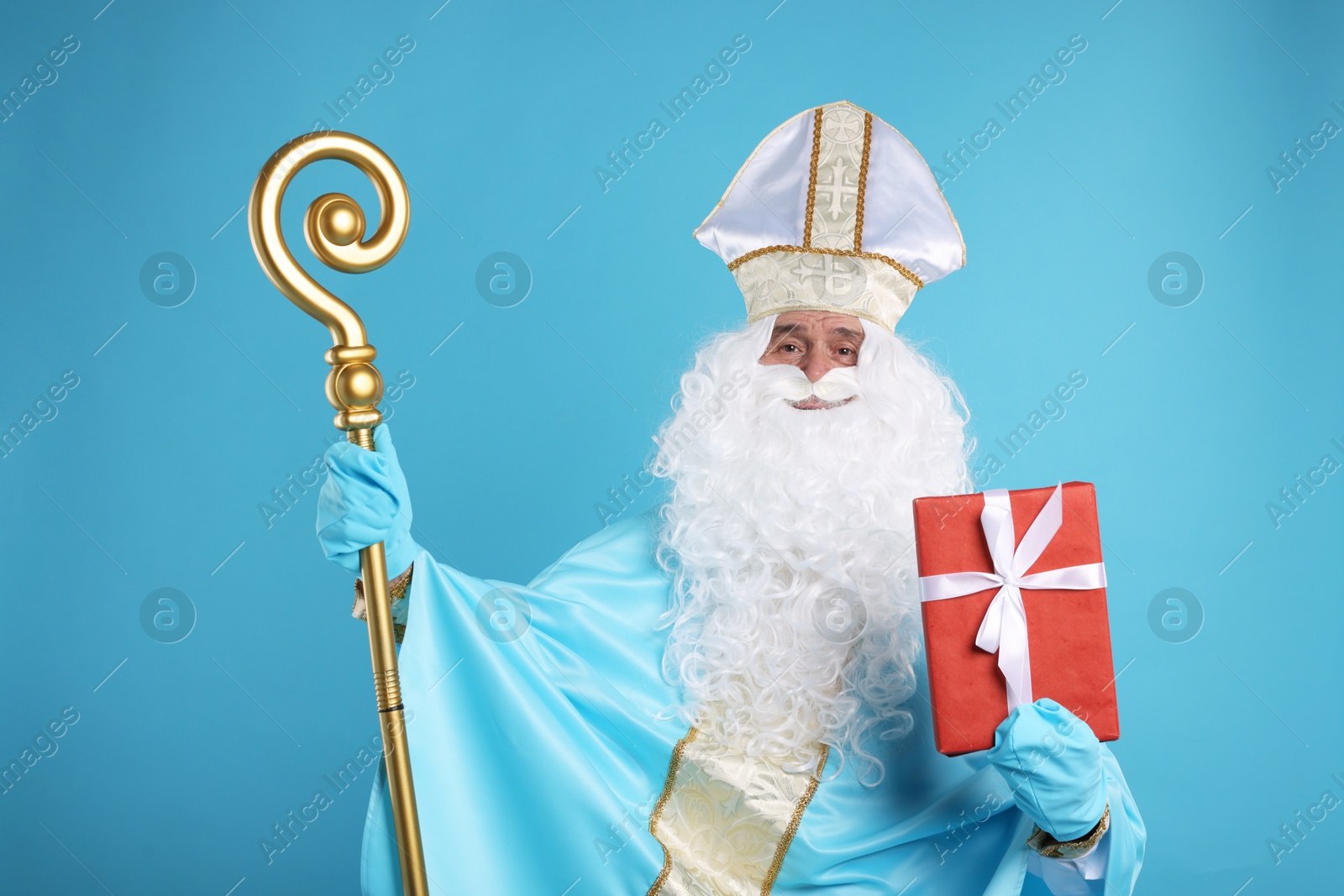 Photo of Saint Nicholas with Christmas gift and crozier on light blue background