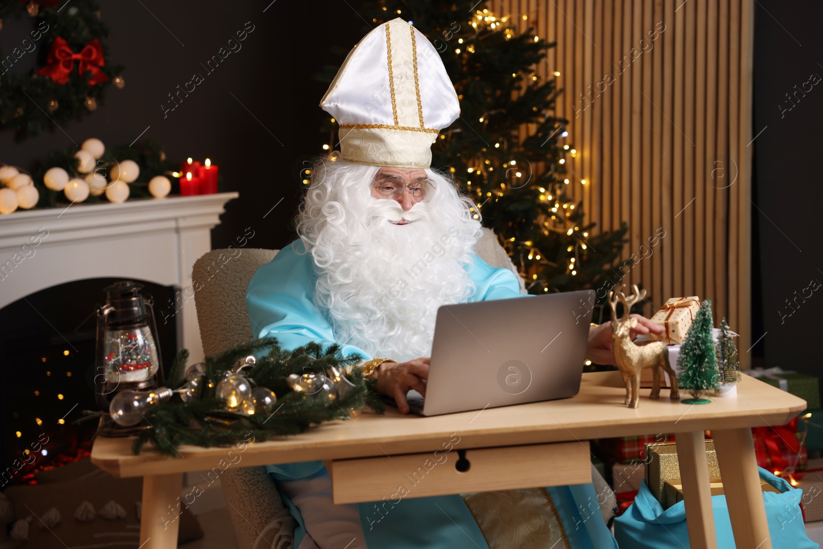 Photo of Saint Nicholas using laptop in room decorated for Christmas