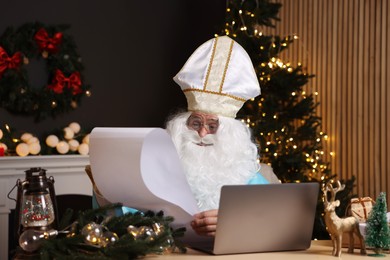 Photo of Saint Nicholas reading wish list in room decorated for Christmas