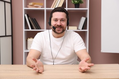 Smiling online speaker in headset streaming webinar at table indoors, view from web camera