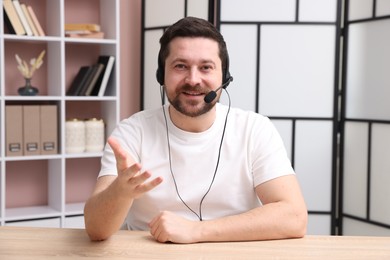 Smiling online speaker in headset streaming webinar at table indoors, view from web camera