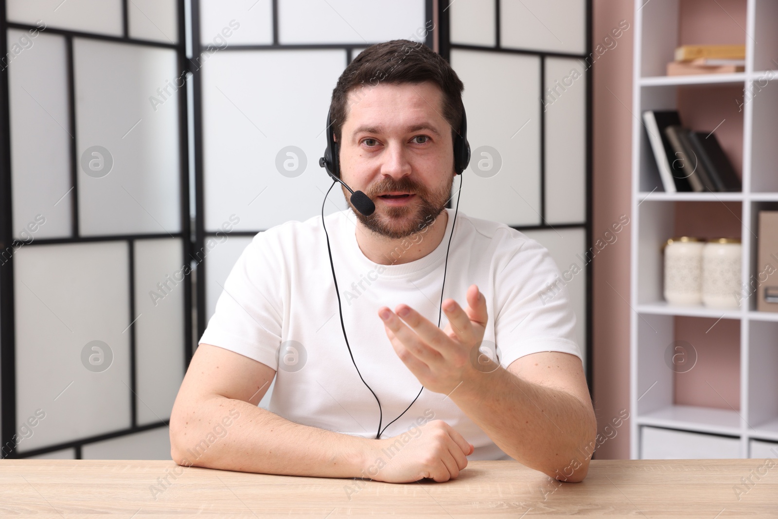 Photo of Online speaker in headset streaming webinar at table indoors, view from web camera