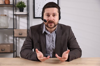 Online speaker in headset streaming webinar at table indoors, view from web camera