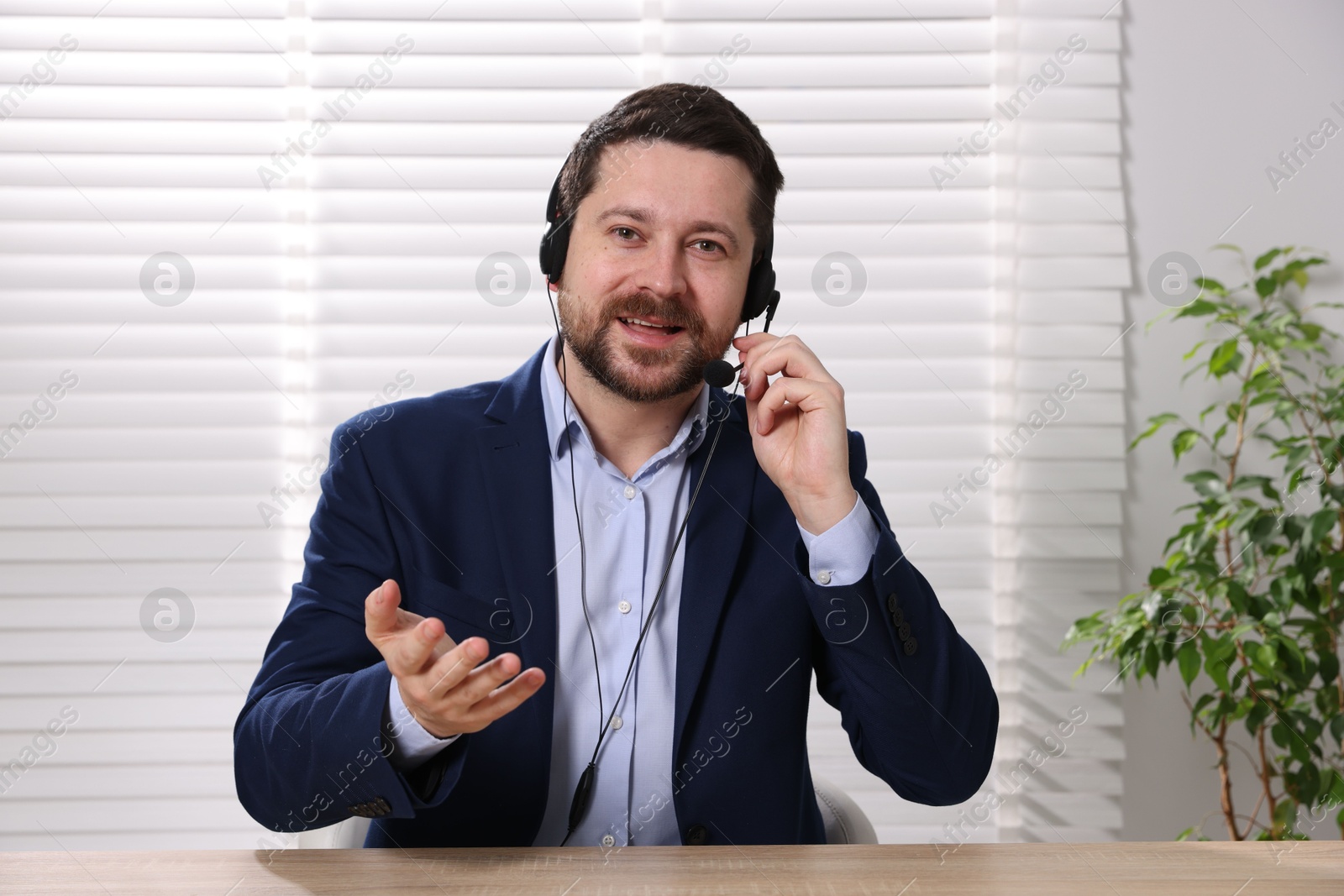 Photo of Smiling online speaker in headset streaming webinar at table indoors, view from web camera