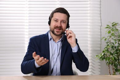 Smiling online speaker in headset streaming webinar at table indoors, view from web camera