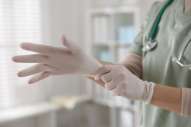 Photo of Medical worker putting gloves in hospital, closeup