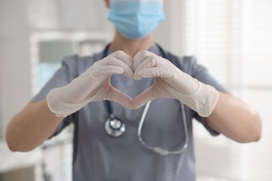 Photo of Medical worker in gloves making heart with hands indoors, closeup