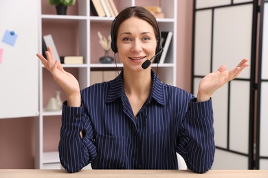 Photo of Smiling online speaker in headset streaming webinar at table indoors, view from web camera