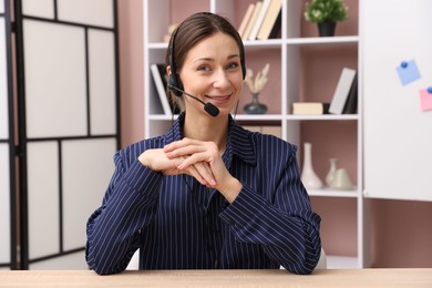 Photo of Smiling online speaker in headset streaming webinar at table indoors, view from web camera