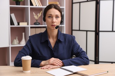 Photo of Online speaker in headset streaming webinar at table indoors, view from web camera