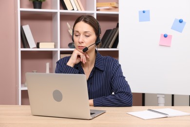 Photo of Online speaker in headset streaming webinar with laptop at table indoors