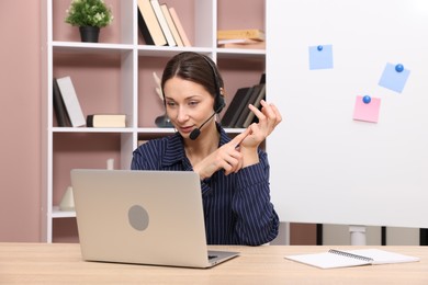 Photo of Online speaker in headset streaming webinar with laptop at table indoors