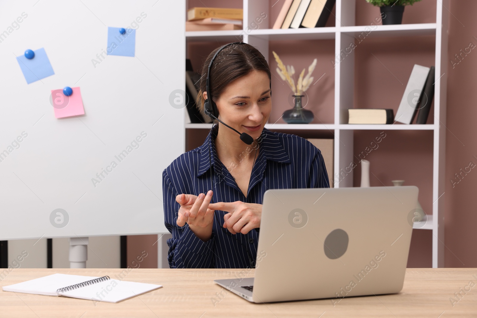 Photo of Online speaker in headset streaming webinar with laptop at table indoors