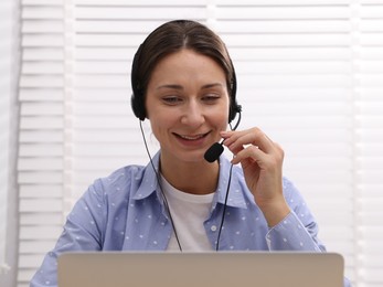 Photo of Smiling online speaker in headset streaming webinar with laptop indoors