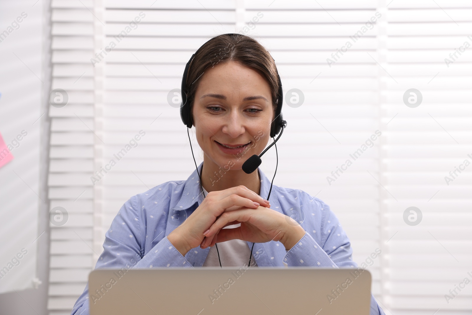 Photo of Smiling online speaker in headset streaming webinar with laptop indoors