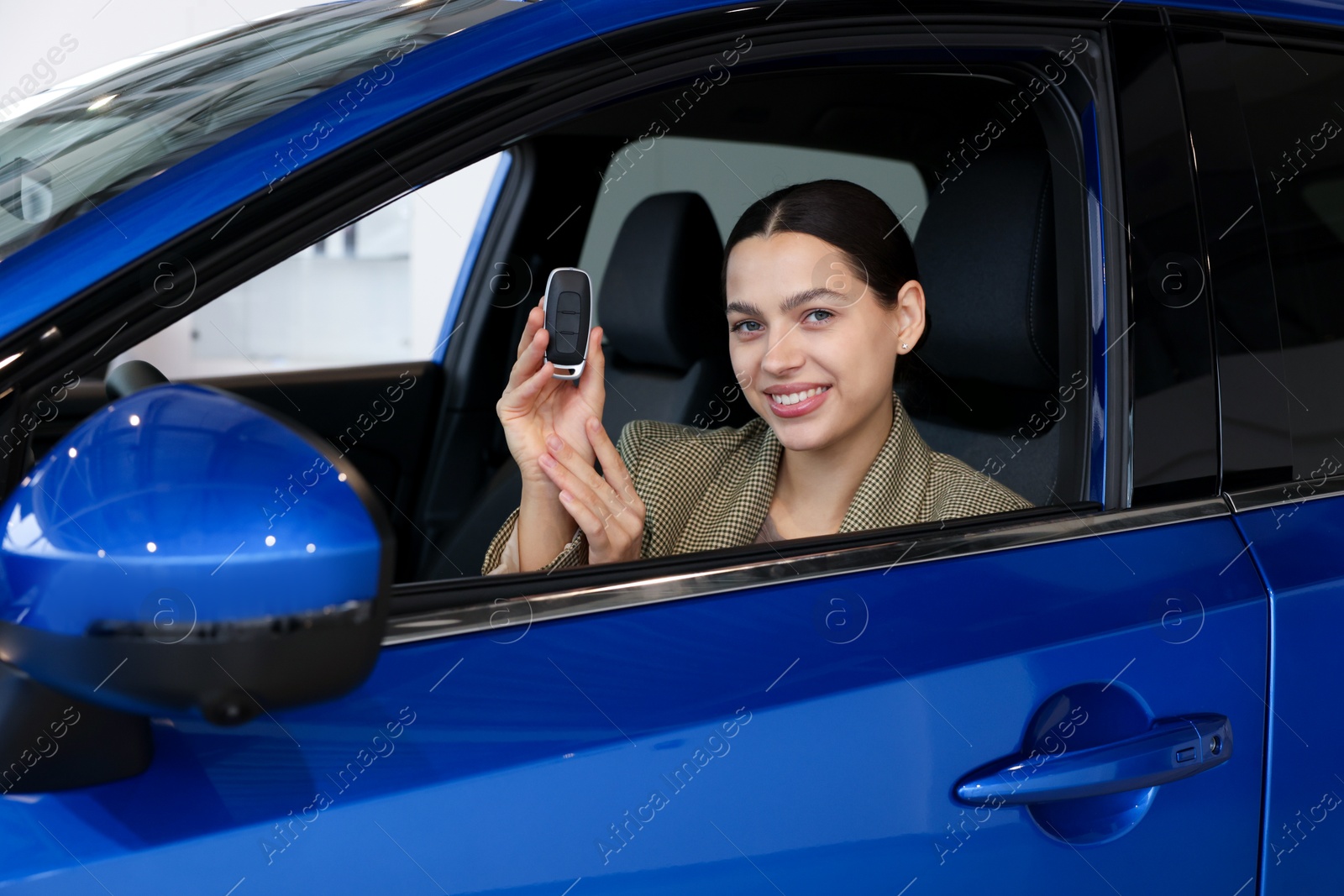 Photo of Happy woman with key inside new car in salon