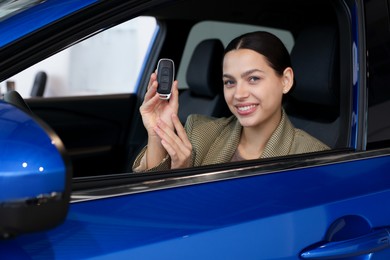 Happy woman with key inside new car in salon