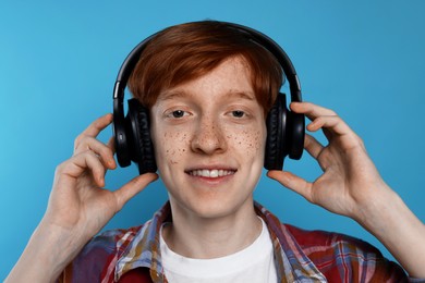 Smiling teenage boy with freckles listening to music by headphones on light blue background