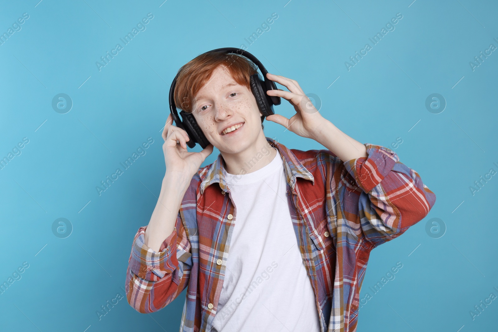 Photo of Smiling teenage boy with freckles listening to music by headphones on light blue background