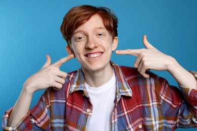 Smiling teenage boy with freckles on light blue background