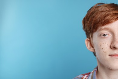 Cute teenage boy with freckles on light blue background, closeup. Space for text