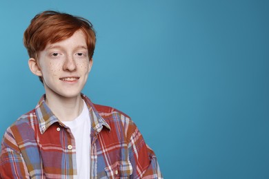 Smiling teenage boy with freckles on light blue background. Space for text