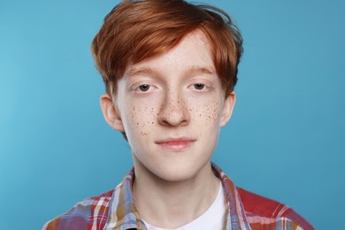 Cute teenage boy with freckles on light blue background, closeup