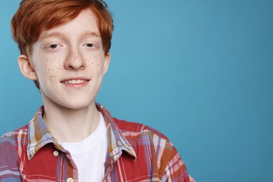 Smiling teenage boy with freckles on light blue background. Space for text