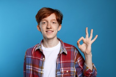 Photo of Smiling teenage boy with freckles showing ok gesture on light blue background