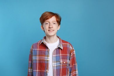 Smiling teenage boy with freckles on light blue background