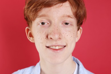 Photo of Smiling teenage boy with freckles on red background, closeup