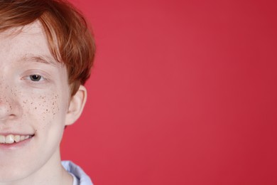 Photo of Smiling teenage boy with freckles on red background, closeup. Space for text