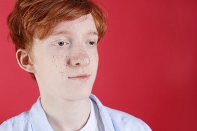 Teenage boy with freckles on red background, closeup. Space for text