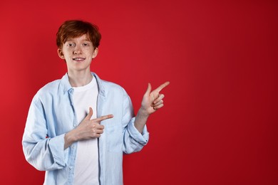 Smiling teenage boy with freckles pointing at something on red background. Space for text