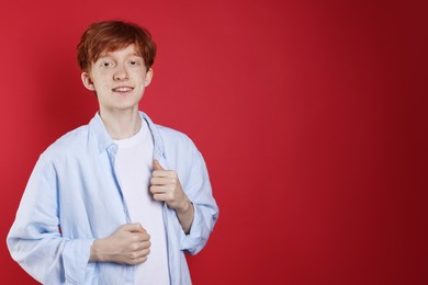 Smiling teenage boy with freckles on red background. Space for text