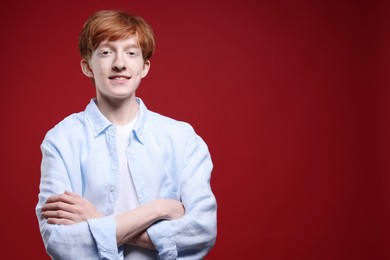 Photo of Smiling teenage boy with freckles on dark red background. Space for text