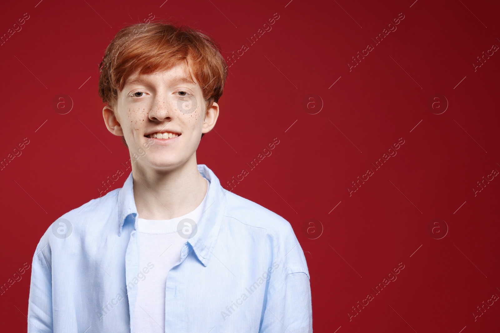 Photo of Smiling teenage boy with freckles on dark red background. Space for text