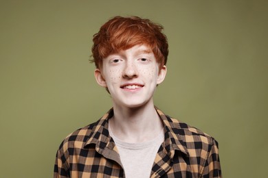 Portrait of smiling teenage boy with freckles on dark green background