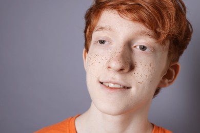 Photo of Smiling teenage boy with freckles on grey background, closeup. Space for text