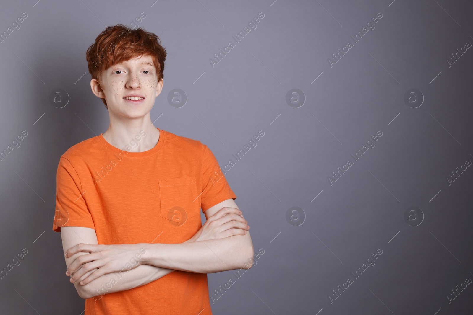 Photo of Smiling teenage boy with freckles on grey background. Space for text