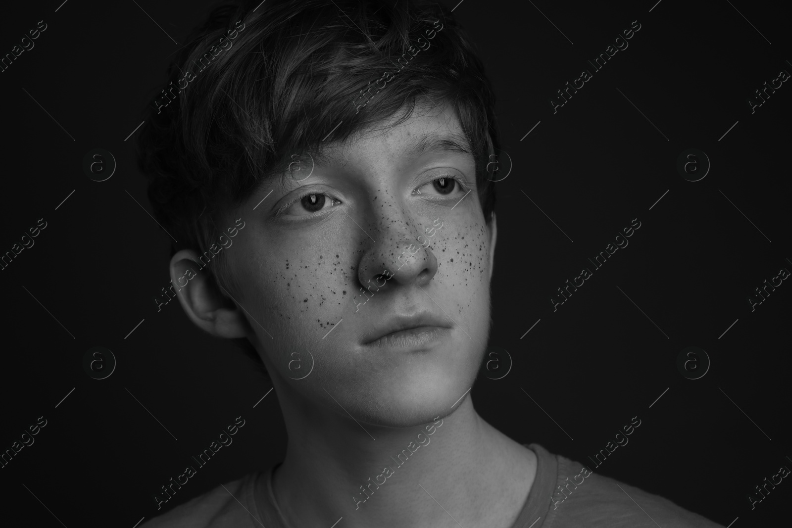 Photo of Teenage boy with freckles on dark background, black and white effect